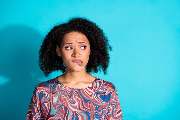 漂亮年轻女孩的照片肖像，咬着嘴唇，神情担忧，穿着时尚多彩的衣服，背景为水绿色。图片下载
