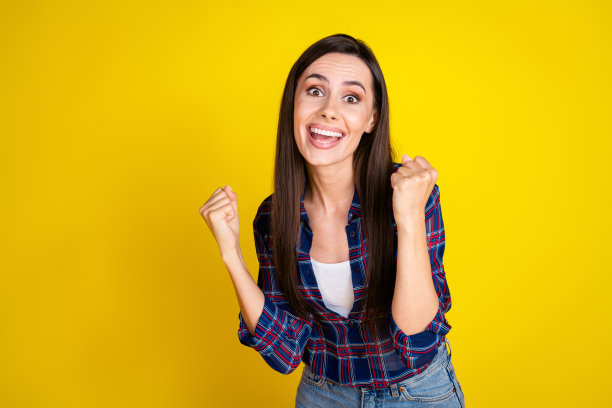 年轻女孩格子时尚装扮黄色背景人像照片，获胜，举起拳头图片下载