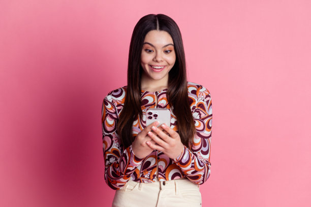 时尚魅力衬衫的拉丁裔棕发少女在粉色背景下手持智能手机发短信的照片肖像图片下载