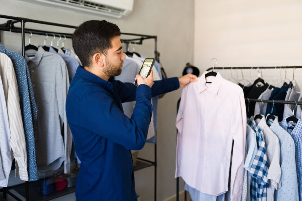 拉丁裔销售员在服装店用智能手机拍摄衬衫的图片，用于在线产品摄影图片下载