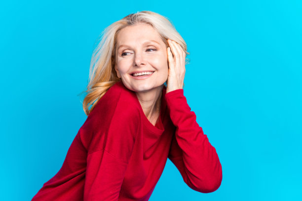 可爱的退休女士的照片肖像，目光空洞，耳后别着头发，穿着时尚的红色服装，背景为蓝色。图片下载