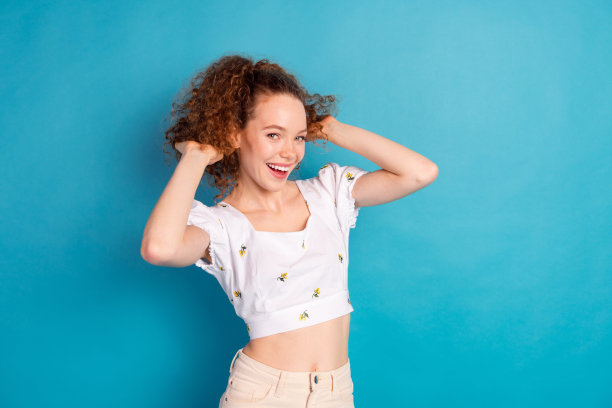 迷人年轻女性的照片肖像，穿着时尚的白色衣服，手触及马尾，背景为蓝色。图片下载