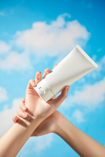 这张护肤产品的宣传图片展示了一位女性模特，双手合十，手中拿着一支无品牌的白色眉膏，背景是晴朗的蓝天。图片下载