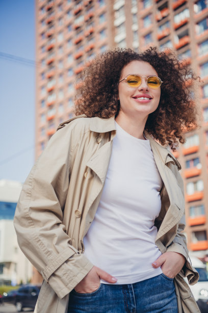 时尚女孩穿着时尚的米色风衣，在阳光明媚的秋季城市户外拍摄的竖版肖像照片图片下载