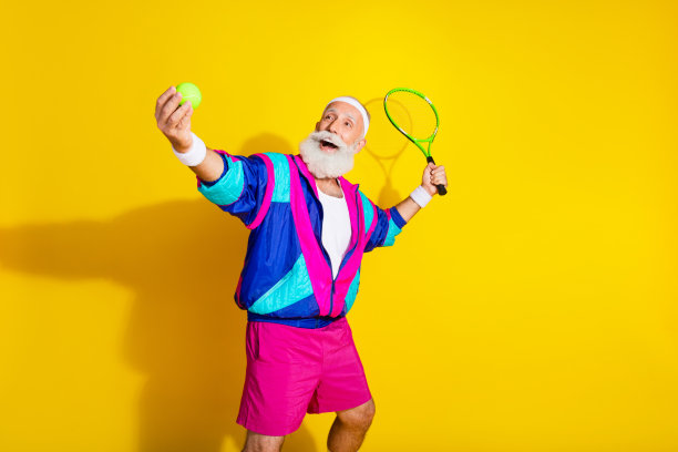 穿着时尚复古运动服的搞笑老年运动员在黄色背景下打网球的照片肖像横幅图片下载
