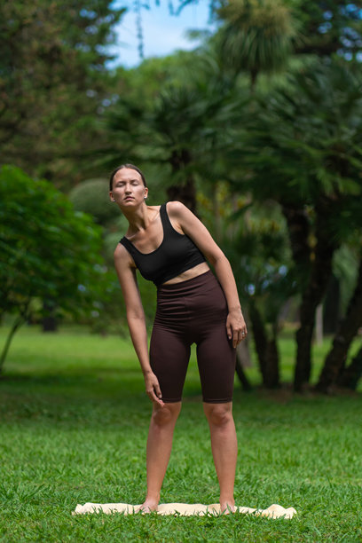 年轻女性在公园的垫子上进行颈部和身体锻炼，智能健身。促进健康和幸福。穿着全套运动服的女孩在公园进行锻炼。竖版照片图片下载