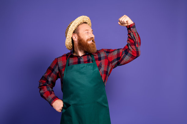 紫色背景上，身穿红色格子衬衫和绿色围裙，展示手臂肌肉的健壮男士农民照片图片下载