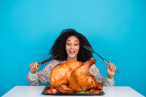 吸引人的年轻女性在蓝色背景下兴奋地切割感恩节晚餐火鸡的照片肖像图片下载
