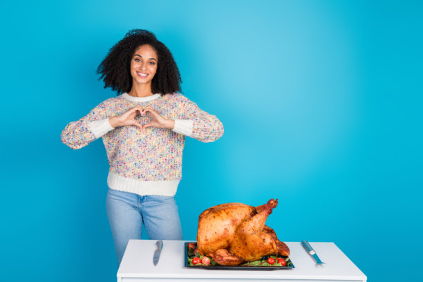 漂亮年轻女孩在蓝色背景下展示心形符号，感恩节晚餐火鸡的照片肖像图片下载