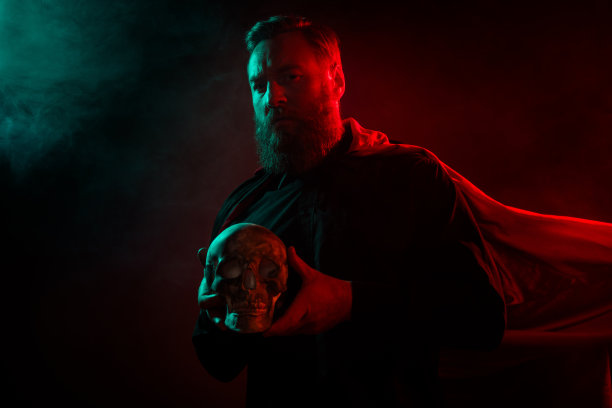 可怕角色的照片，恐怖男子手持人类头骨，背景是黑暗、雾气弥漫、神秘的场景。图片下载