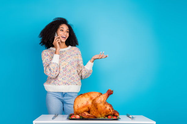 年轻女性的照片肖像，正在打电话，目光投向空旷的空间，庆祝感恩节晚餐，背景为蓝色，桌上有火鸡。图片下载