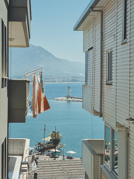 透过城市房屋的多重墙壁，可以看到大海、山脉和白色灯塔的竖版照片。旅游、海滨假期、海滩度假的概念。图片下载