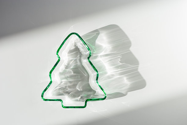 绿色玻璃制成的新年树，阳光下的圣诞树，投射出美丽的阴影和阳光的闪耀，背景为灰色。冬季假日概念，极简抽象美学照片。图片下载