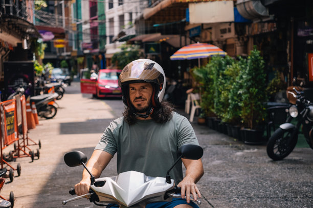 中年男子在东南亚戴露脸头盔驾驶摩托车的横版照片图片下载