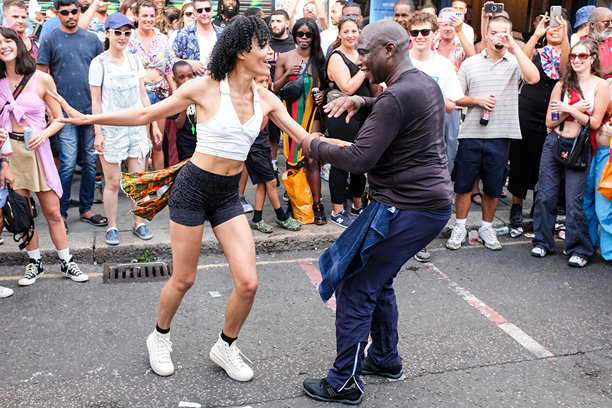 诺丁山狂欢节。伦敦 candid 照片 2022。街头狂欢者享受生活。两位节日参与者在街上与旁观者一起跳舞。图片下载