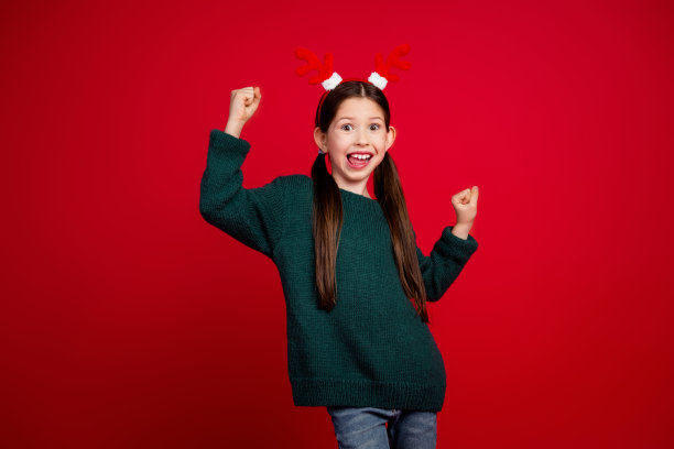 穿着绿色圣诞主题服装、在红色背景下庆祝胜利的漂亮小女孩照片图片下载
