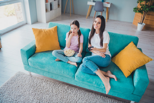 快乐的家庭照片，可爱的妈妈和女儿在舒适的客厅里享受周末时光，一起看电影。图片下载