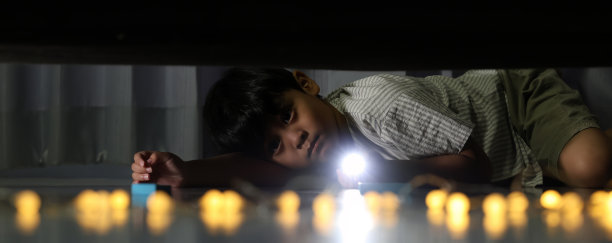 男孩用手电筒查看床下。晚上，孩子害怕怪物，手握手电筒照亮床下，查看地面，检查是否有鬼魂。图片下载