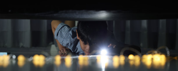 男孩用手电筒查看床下。晚上，孩子害怕怪物，手握手电筒照亮床下，查看地面，检查是否有鬼魂。图片下载