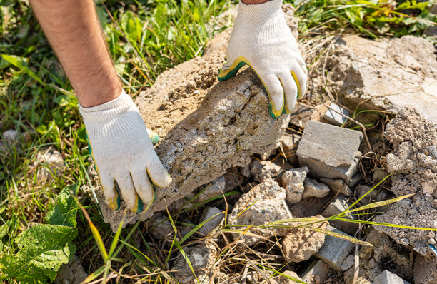 一双戴着白手套的手握着一块大块破碎的混凝土。建筑废料的处理。这张图片捕捉了体力劳动的强度。图片下载