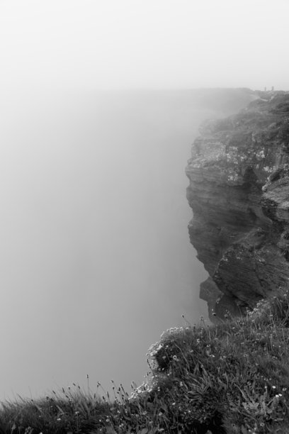 黑白照片展示了爱尔兰克莱尔郡的莫赫悬崖，陡峭的悬崖面在浓厚的雾气中逐渐消失。单色效果突显了雾霭景观的鲜明纹理和阴郁氛围。图片下载
