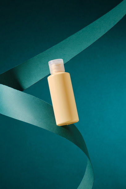 这张模板照片展示了一只躺在卷曲绿色丝带上的黄色瓶子，背景为深绿色，非常适合展示美容产品或品牌形象。图片下载