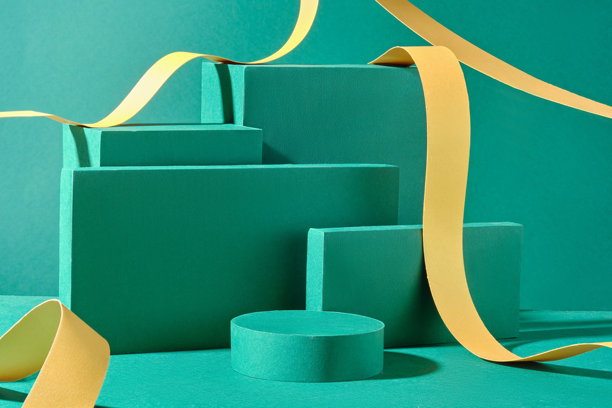 产品广告图片模板展示了一个圆形和四个矩形的讲台，前面有空位，装饰着流动的黄色丝带，背景为绿色。图片下载