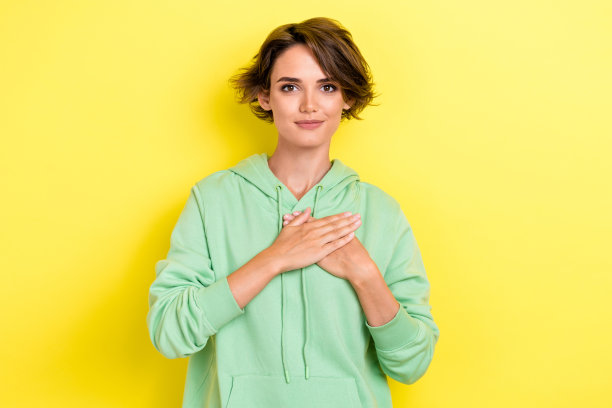 迷人年轻女性的照片肖像，双臂抱胸，关注心脏健康，支持心脏慈善事业，穿着时尚的绿色服装，背景为黄色。图片下载