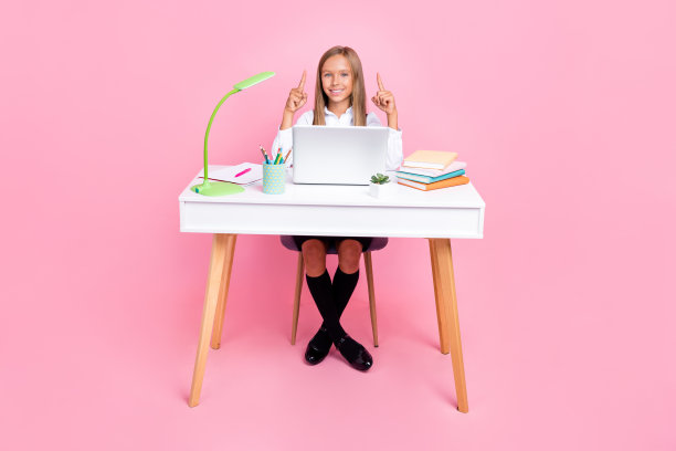 穿着校服的快乐聪明女学生在粉色背景上指向空旷的地方的全身照片图片下载