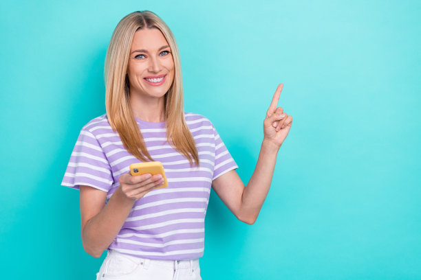 可爱的女企业家特写照片，手指指向空白处，手持手机，进行电子商务交易，背景为水绿色。图片下载