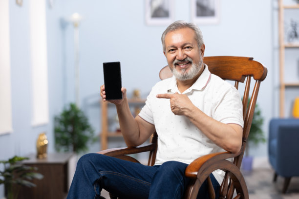 老年男子坐在摇椅上放松，使用手机的家庭生活照片图片下载