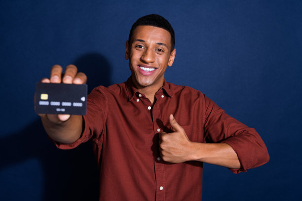 照片时髦的酷家伙穿着棕色衬衫，显示银行卡显示拇指向上孤立的蓝色背景图片下载