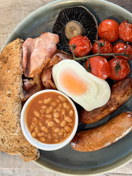 特写图片:一盘油炸早餐食材，两根香肠，烤豆，葡萄藤上的圣女果，煎蛋，大波多贝罗蘑菇，培根片，烤全麦面包，木纹背景，高架视图图片下载