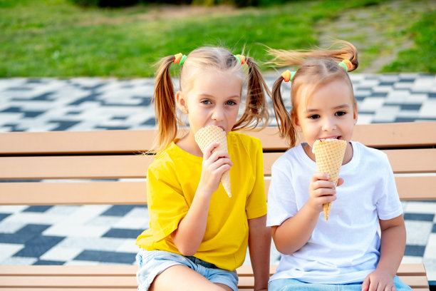 孩子们女孩们在公园的绿色草坪上吃着夏天的冰淇淋，一张明亮的夏天儿童假期的照片，两个小女孩朋友在夏天欢笑和玩耍。图片下载