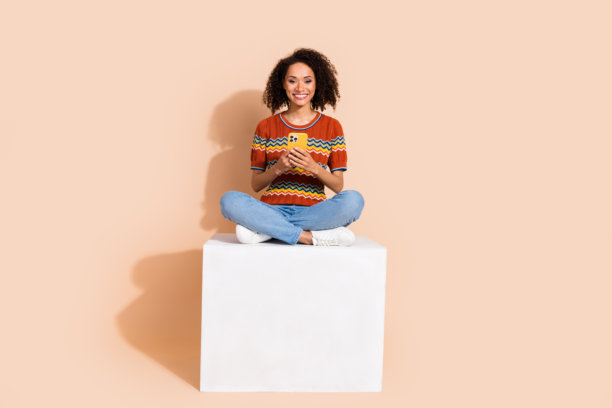 穿着t恤的聪明女孩的全身照片，坐在平台上，拿着智能手机阅读电子邮件，孤立在柔和的颜色背景下图片下载