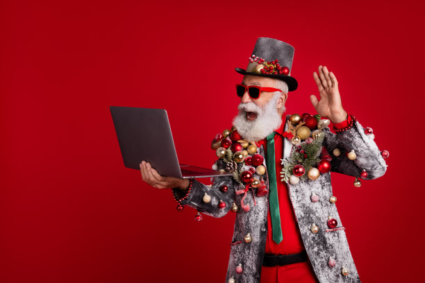 圣诞老人的照片有趣的人拿着上网本视频电话挥手hi穿着圣诞树球服装太阳镜孤立的红色背景图片下载