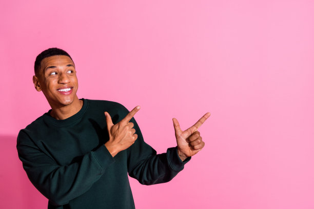 照片中，有魅力的搞笑小伙穿着运动衫，露出两根手指空白的空间，孤立的粉红色背景图片下载