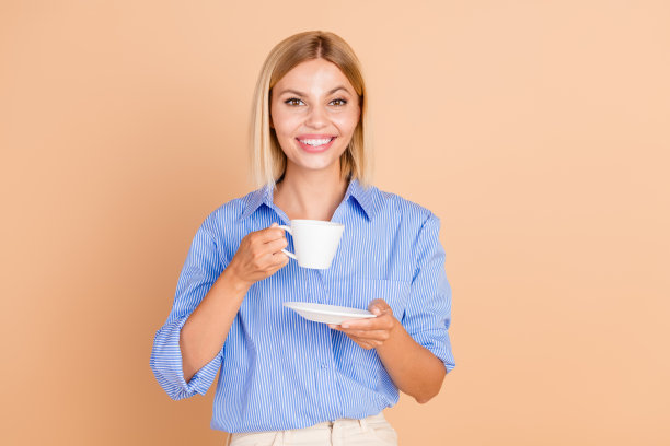 照片中可爱可爱的女孩早上穿蓝色衬衫喝空空间孤立米色背景图片下载