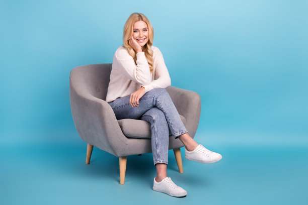 照片中开朗漂亮的女人穿着时髦的白色衣服，坐在蓝色背景的椅子上图片下载