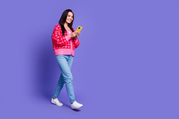 迷人积极的女人穿粉红色开衫打字现代小工具空白空间隔离紫色背景的全长照片图片下载