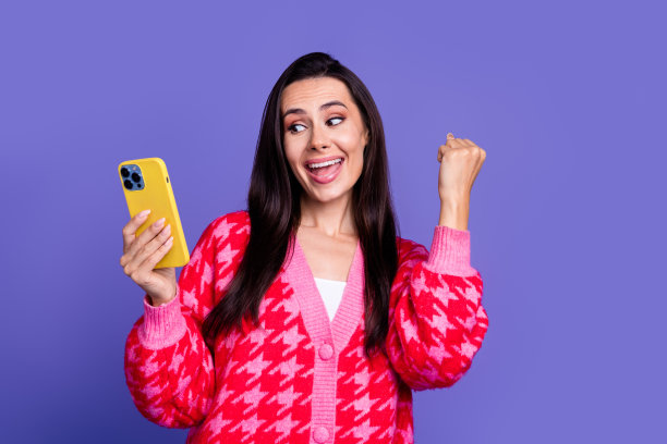 可爱的幸运女孩穿粉红色开衫赢得游戏的照片现代小工具孤立的紫色背景图片下载