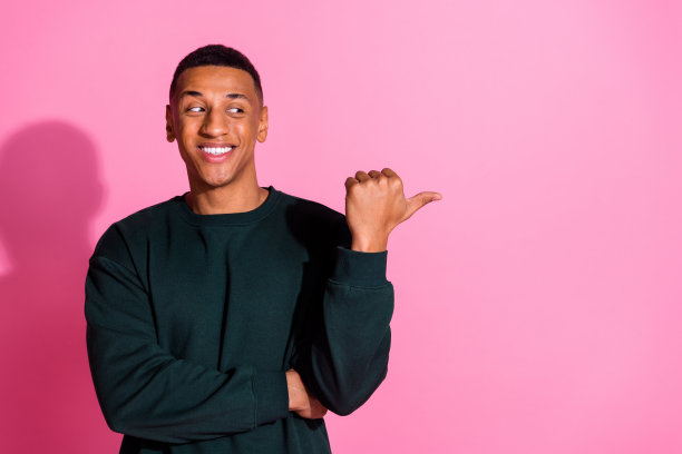 照片上有魅力有趣的家伙穿着运动衫，用拇指指着空旷的空间孤立的粉红色背景图片下载