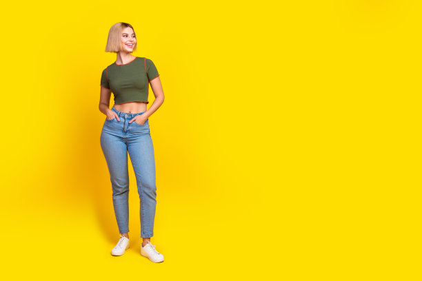 正面可爱的女孩穿着卡其布t恤牛仔裤的全长照片，在黄色背景上提供孤立的空间图片下载