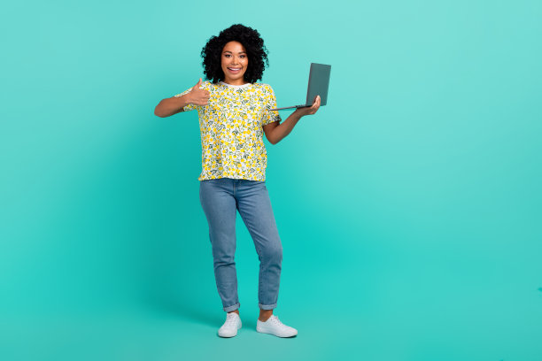 漂亮的年轻女子上网本拇指向上穿t恤孤立的蓝绿色背景的全尺寸照片图片下载