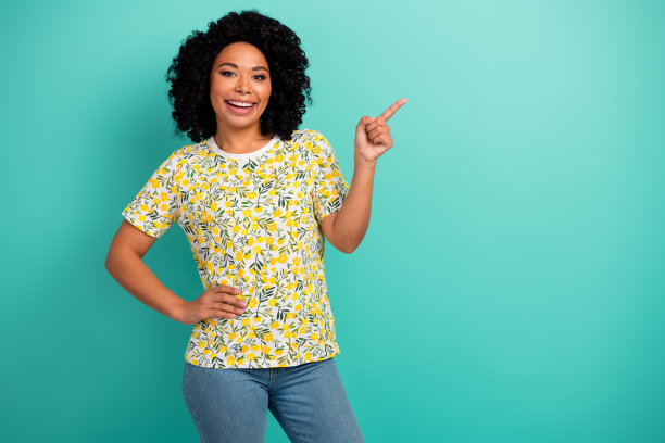 照片中穿着黄色t恤的开朗漂亮的女士用手指着空白的空间孤立的蓝绿色背景图片下载