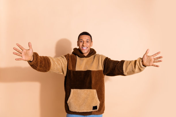 照片中，开朗善良的男人穿着时尚的衣服，张开双手拥抱在米色背景上图片下载