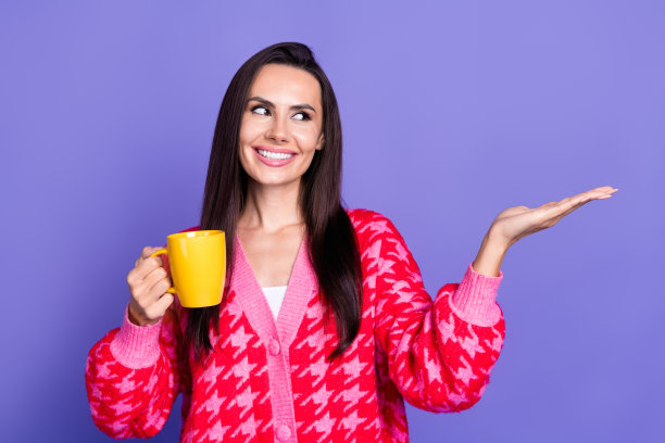 开朗漂亮的女士穿着粉红色的开襟羊毛衫喝茶的照片，显示手臂空白，孤立的紫罗兰色背景图片下载