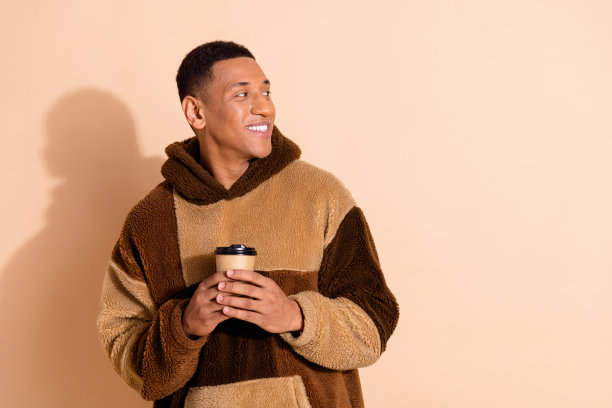 照片中开朗帅气的男子穿着时髦的衣服，拿着咖啡杯，在米色背景上显得空空荡荡图片下载