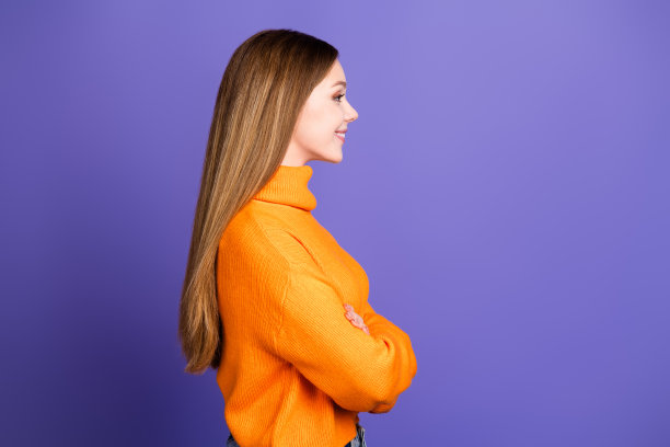 侧照片十几岁的金发女孩在橙色高领毛衣折叠双手自信地看着copyspace孤立的紫色背景图片下载