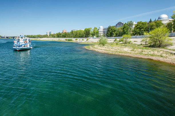 这张照片捕捉了一个宁静的河流场景，一只小船或河流电车在平静的蓝色水面上缓缓移动。船身涂成白色和蓝色，随着它远离镜头，轻轻地激起涟漪。图片下载